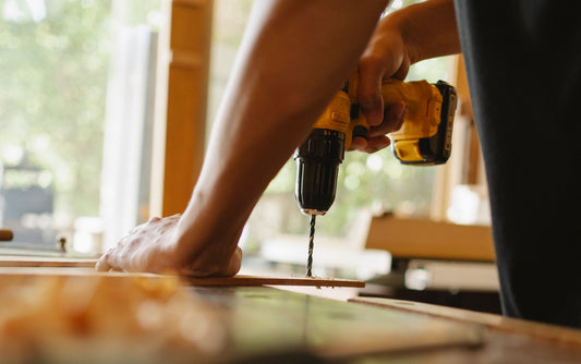 Una persona fora una tavola di legno con un trapano e una punta elicoidale.