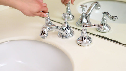 Una mano gira il comando di un rubinetto cromato sopra un lavabo.