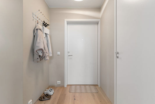 Ingresso luminoso di un appartamento con porta, ganci appendiabiti e pavimento in legno