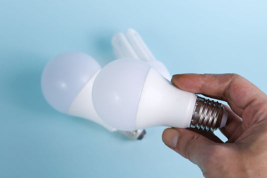 Mano che tiene una lampadina LED opaca con attacco a vite visibile su sfondo azzurro