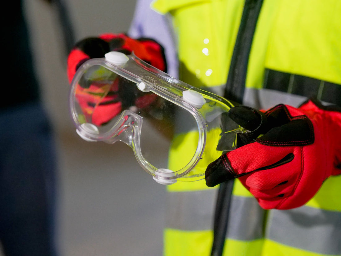 Mani con guanti da lavoro che tengono occhiali di protezione a mascherina trasparente